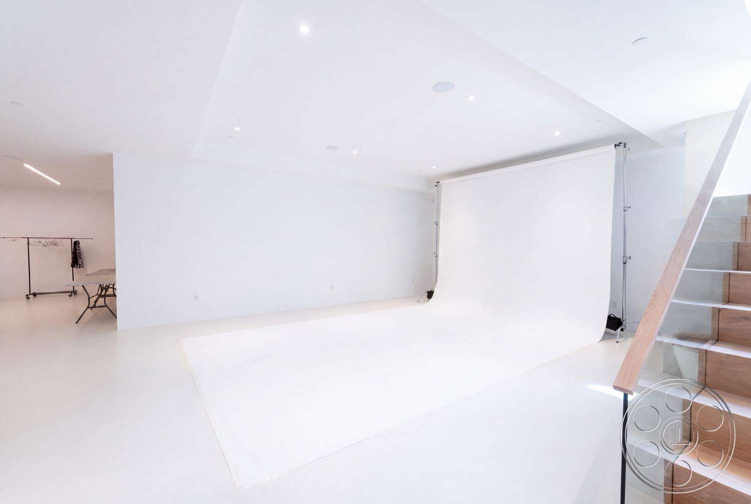 Modern 535 - recessed lighting, minimalist design, concrete flooring, folding table, white seamless backdrop, white painted walls, metal clothing rack, wooden staircase with glass railing