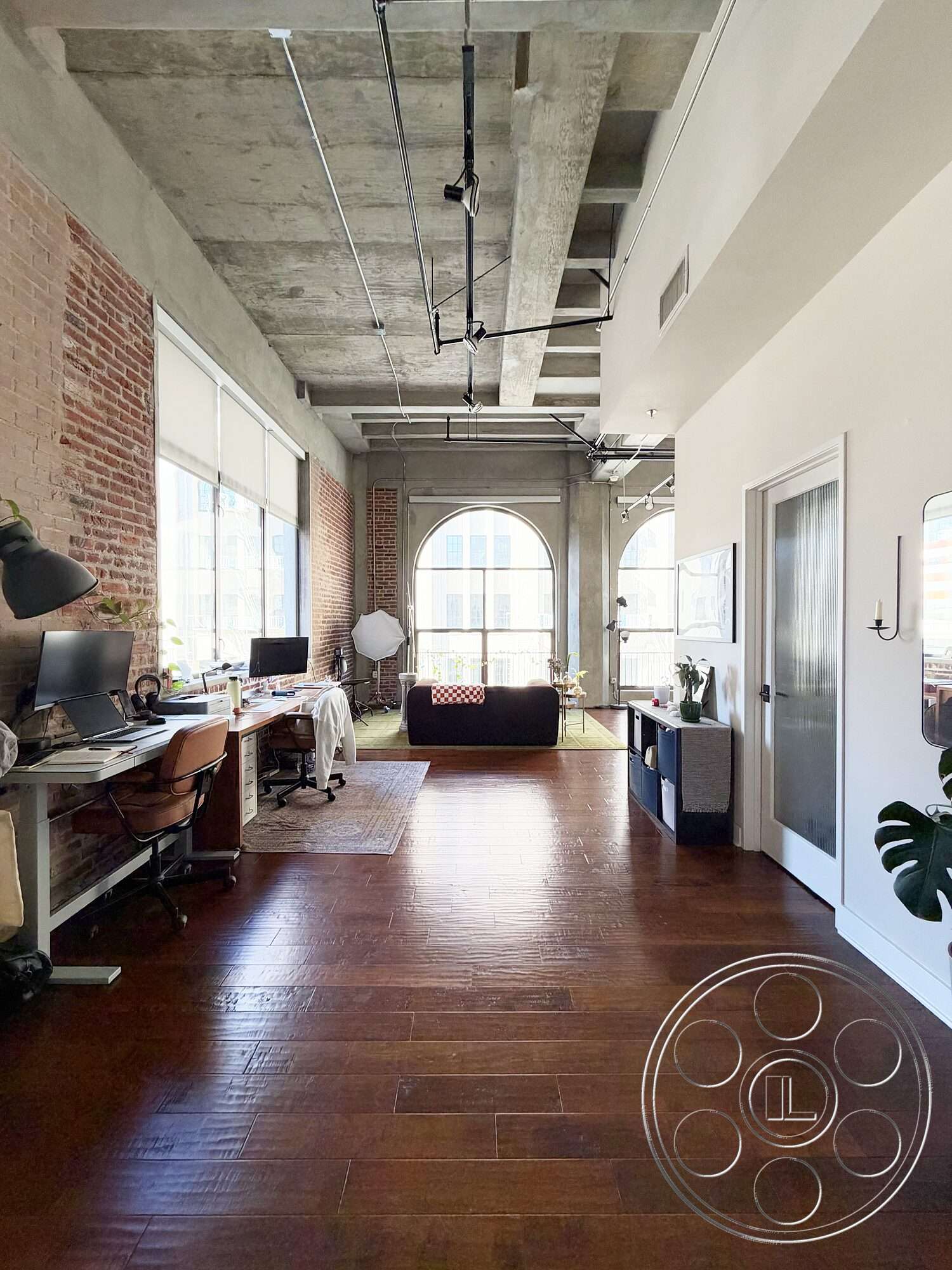 Brockman 310 - hardwood flooring, open floor plan, minimalist furniture, floor-to-ceiling windows, industrial lighting fixtures, concrete ceiling, natural light setting, exposed brick accent wall, arched window design, modern home office area, urban apartment