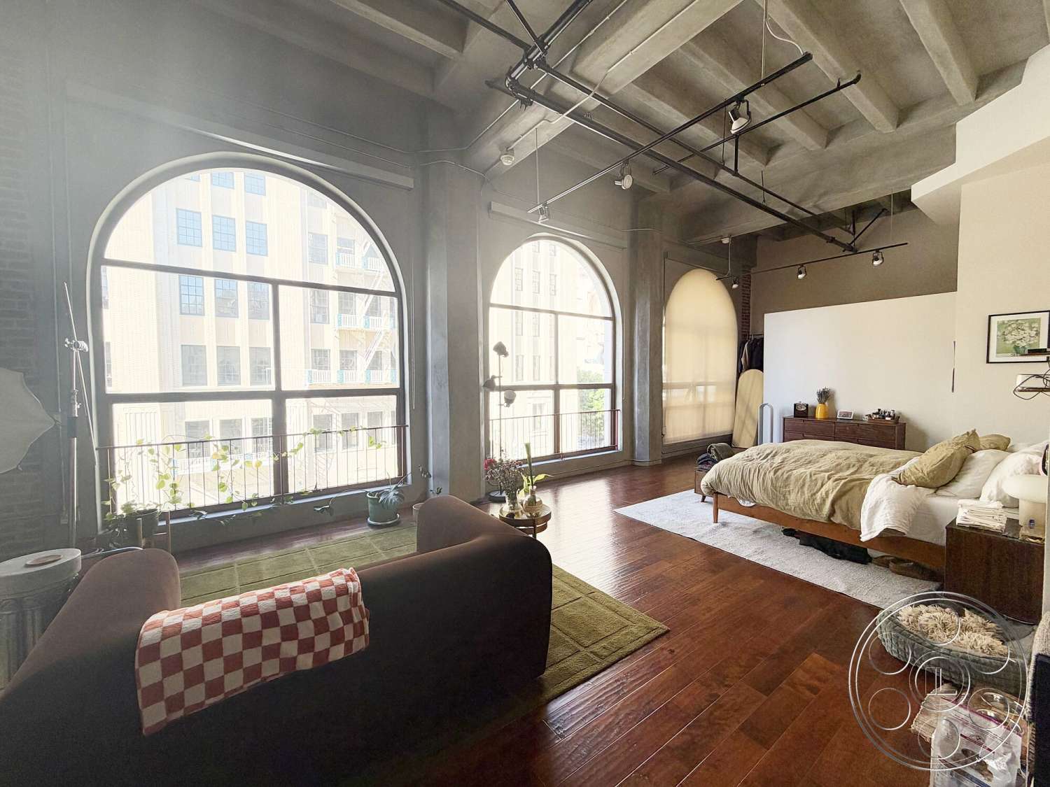 Brockman 310 - minimalist decor, neutral color palette, large windows, natural light, decorative plants, wooden dresser, area rug, city view, sitting area, track lighting, soft bedding, textured plaster walls, open living space, exposed concrete ceiling, arched windows, hardwood bedroom floors, glass balcony railing, industrial style loft