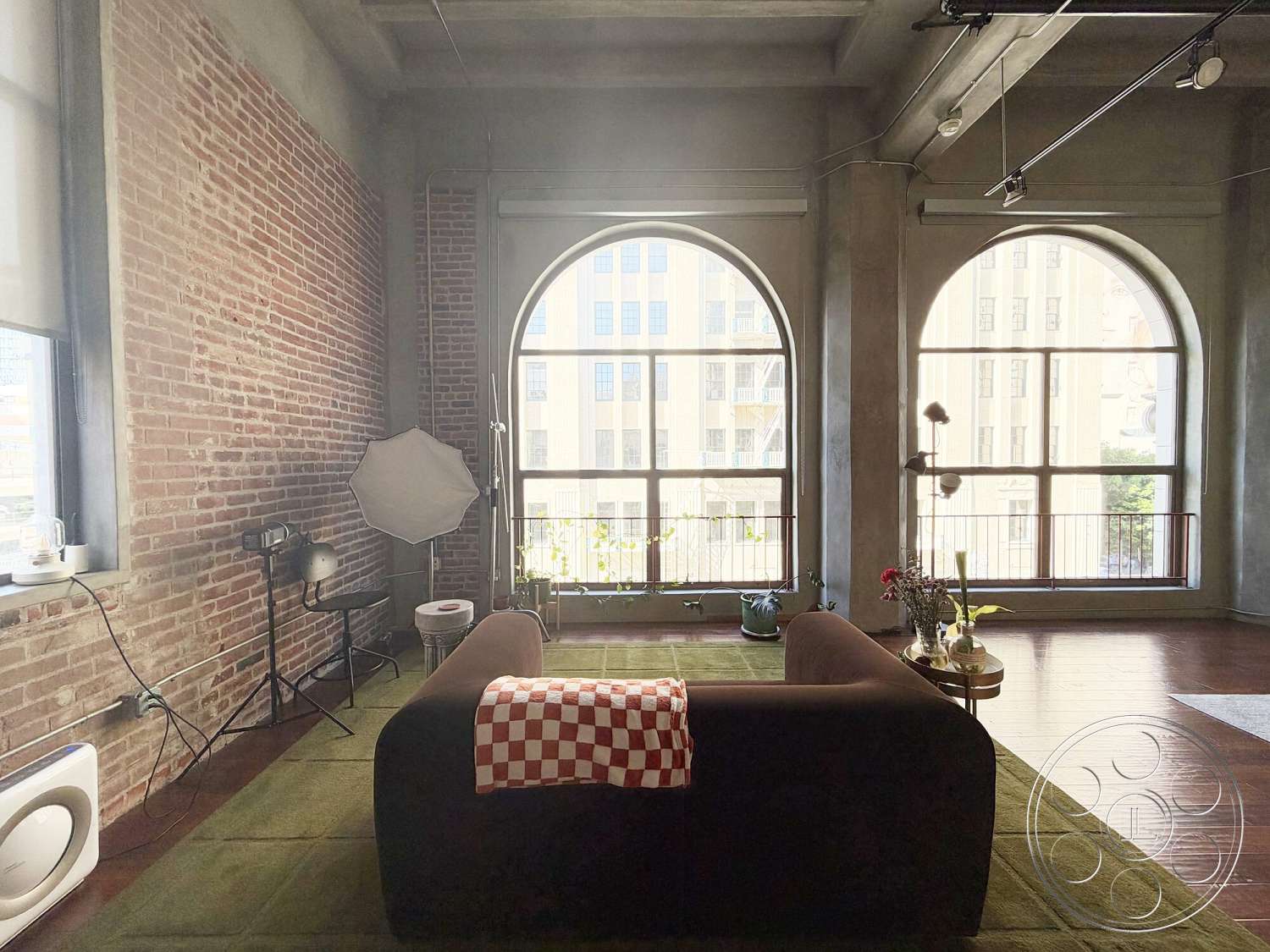 Brockman 310 - hardwood flooring, open space layout, industrial lighting fixtures, arched windows, green area rug, concrete ceilings, exposed brick accent wall, corner sofa with red and white checkered throw