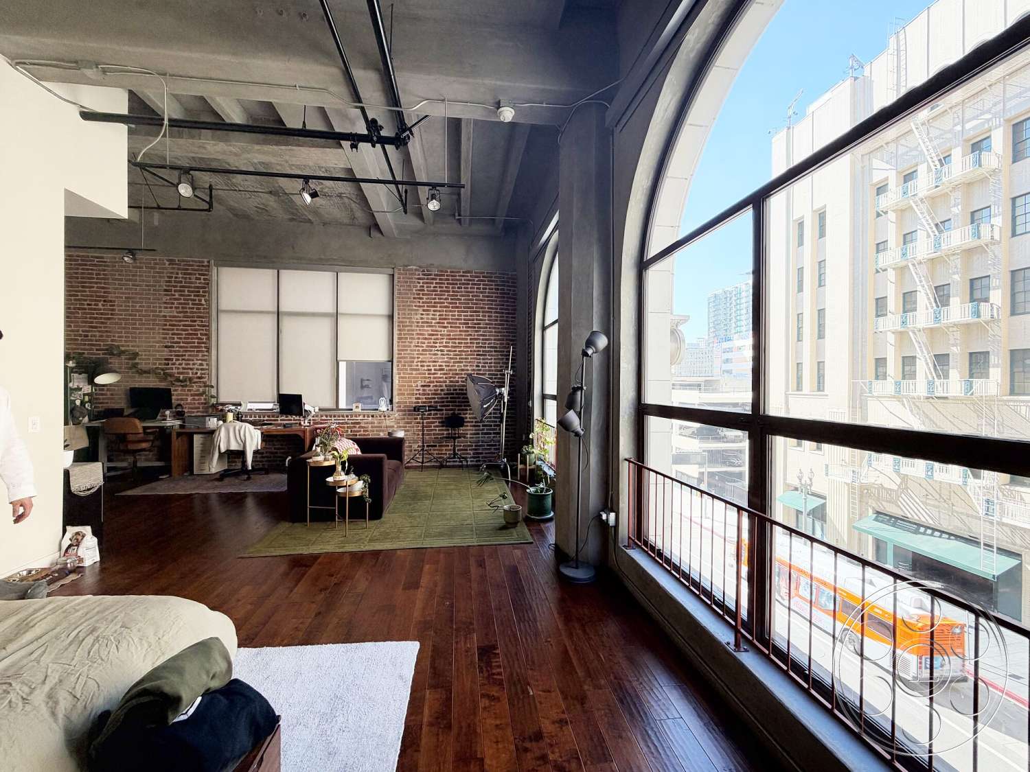 Brockman 310 - natural light, open layout, modern furniture, urban setting, concrete ceiling, large arched windows, green area rug, metal floor lamp, hardwood living room floors, exposed brick accent wall, industrial interior, contemporary office workspace