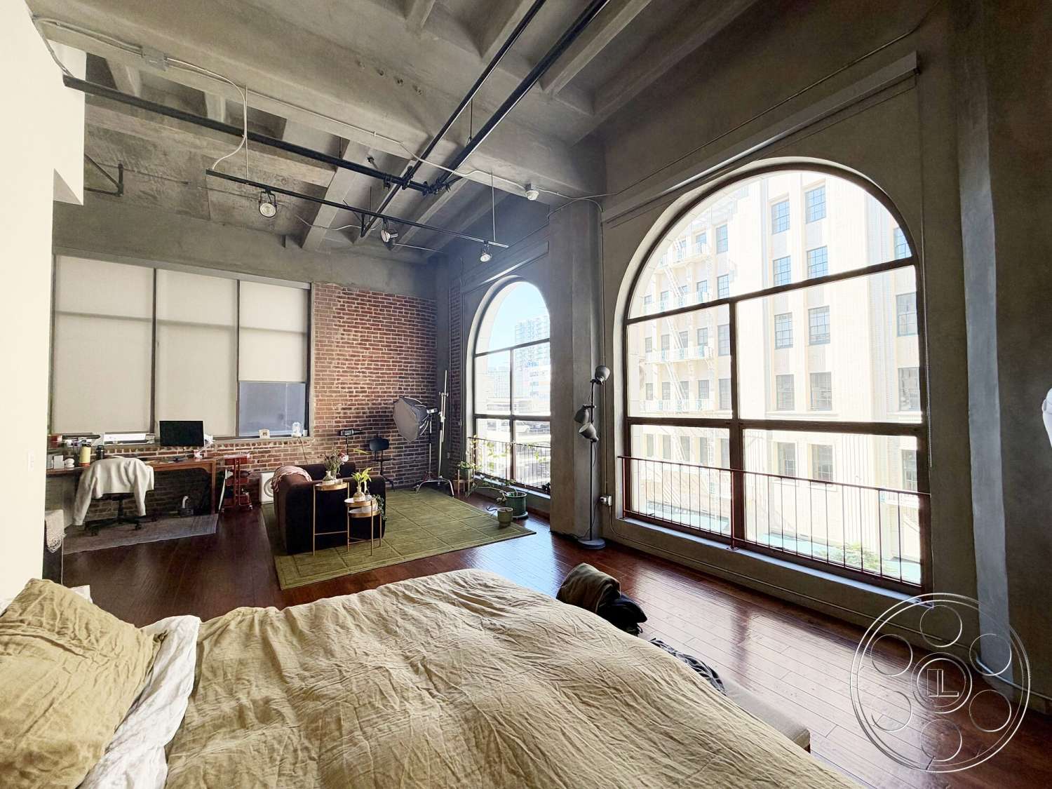 Brockman 310 - open floor plan, modern workspace, arched windows, green area rug, designer furniture, steel railings, hardwood bedroom floors, exposed brick accent wall, large window views, urban loft setting, concrete loft ceiling, industrial style ceiling lamps, bedroom with textured bedding