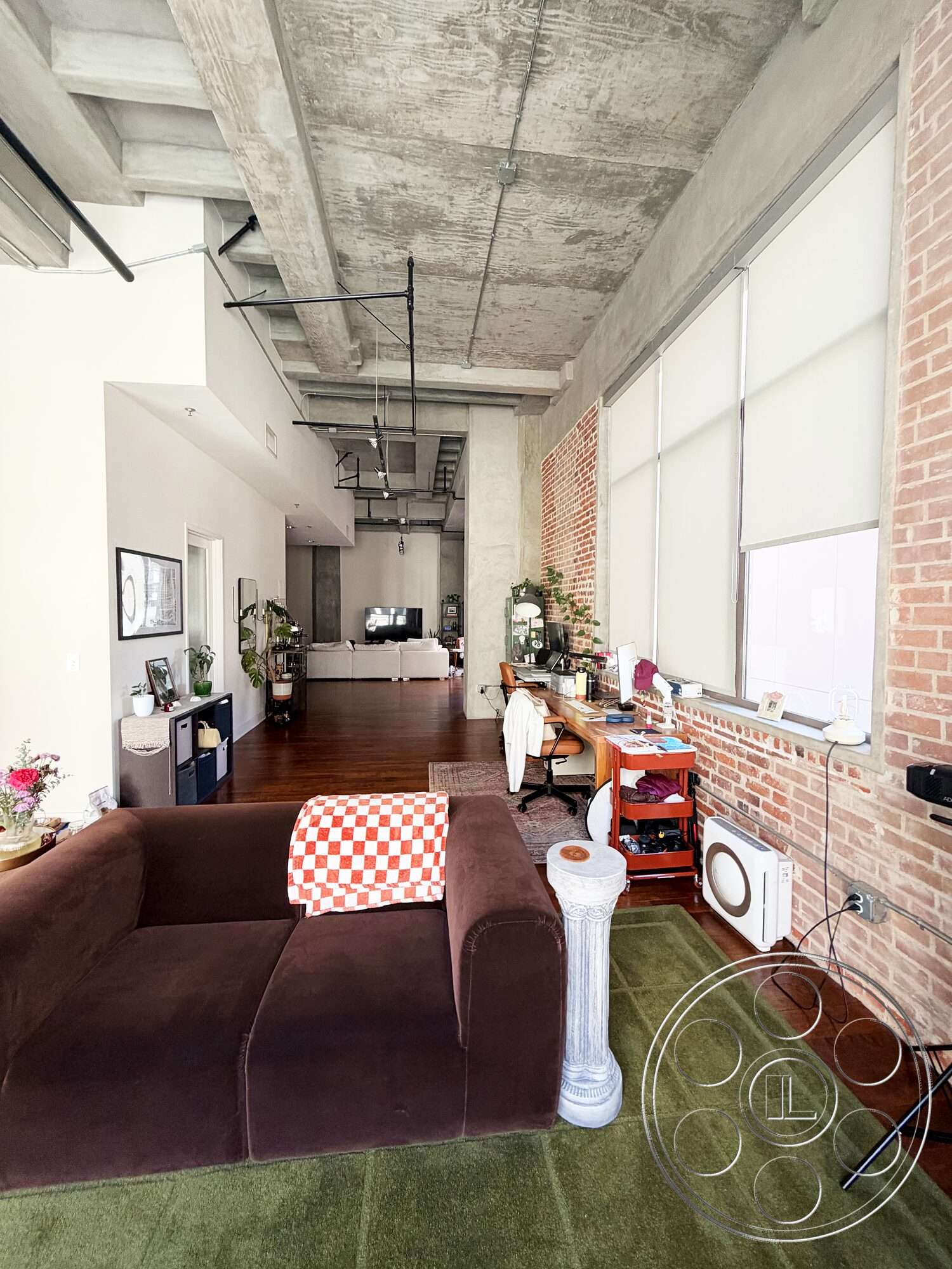 Brockman 310 - minimalist decor, contemporary style, open floor plan, modern furniture, exposed concrete ceiling, green area rug, industrial light fixtures, wooden accent table, exposed brick accent wall, large windows with blinds, plush brown sectional sofa, dark hardwood living room floors, checkered throw pillow, stylish decorative elements