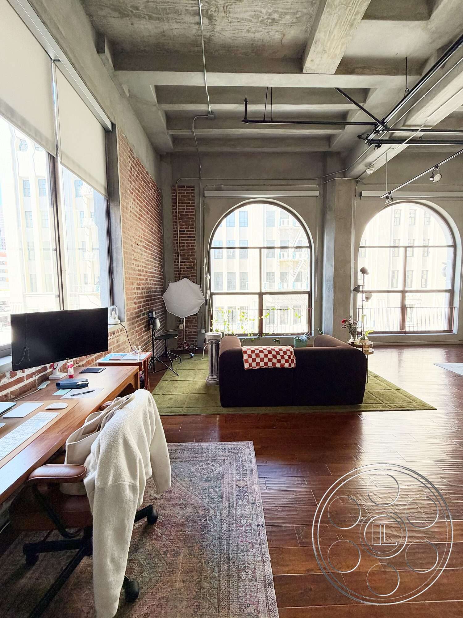 Brockman 310 - hardwood flooring, industrial lighting fixtures, concrete ceiling, large arched windows, green area rug, exposed brick accent wall, open concept interior, plush upholstered sofa, rectangular living room layout, modern desk workspace