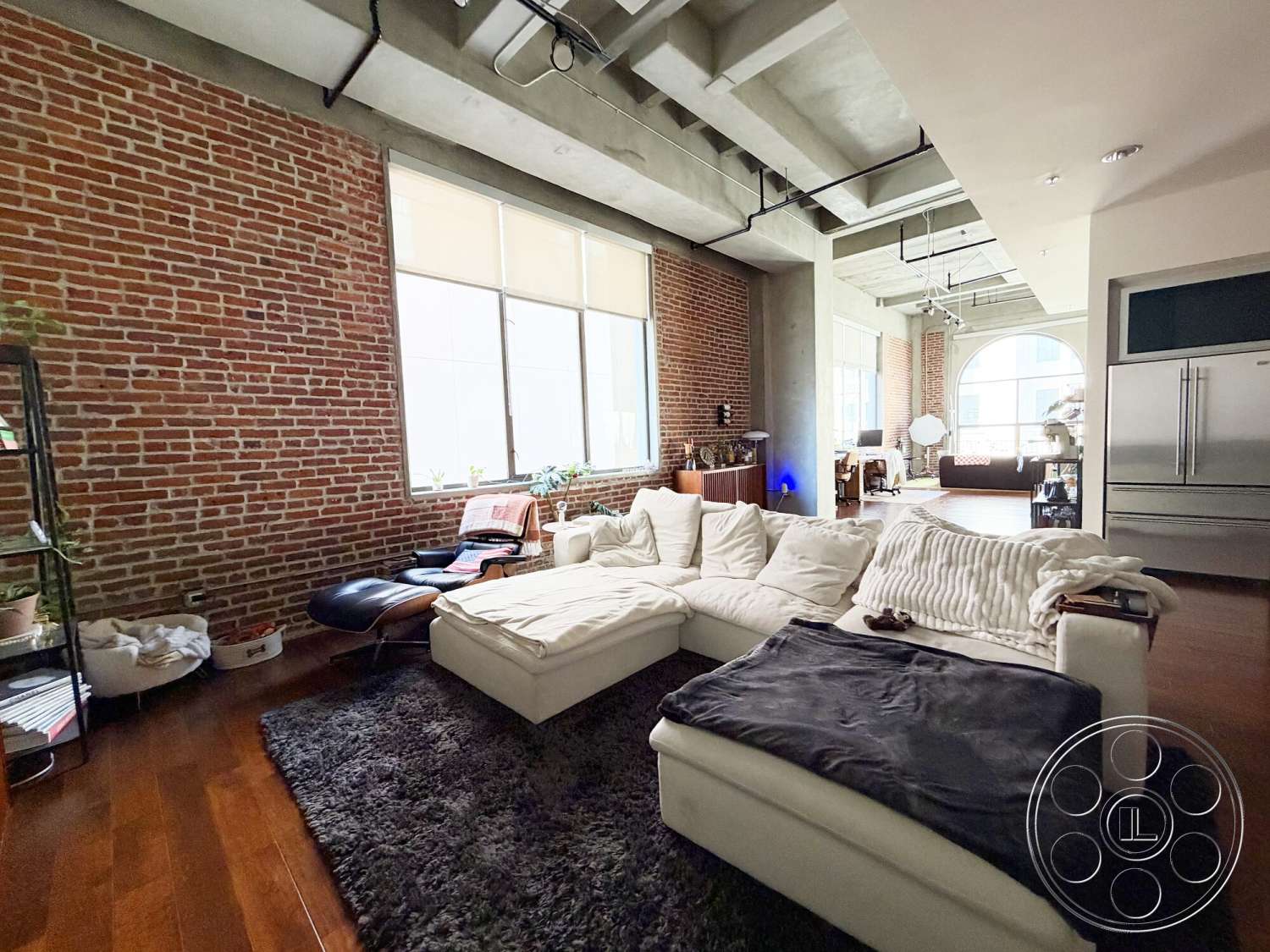Brockman 310 - hardwood flooring, metal shelving unit, floor-to-ceiling windows, urban loft, dark area rug, open concept living space, concrete ceiling, modern sectional sofa, exposed brick accent wall, industrial-style lighting fixtures, spacious interior layout, arc-shaped windows