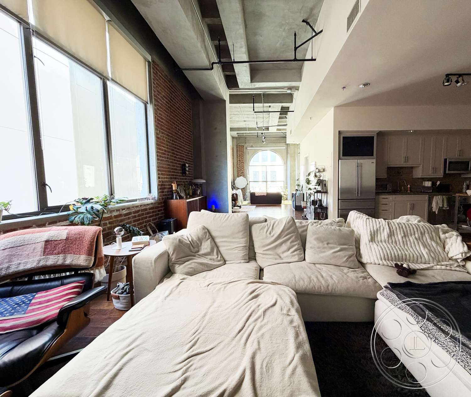 Brockman 310 - open floor plan, concrete ceiling, stainless steel kitchen appliances, hardwood living room floors, recessed lighting fixtures, modern sectional sofa, exposed brick accent wall, urban loft setting, district-style windows, kitchen with built-in cabinets
