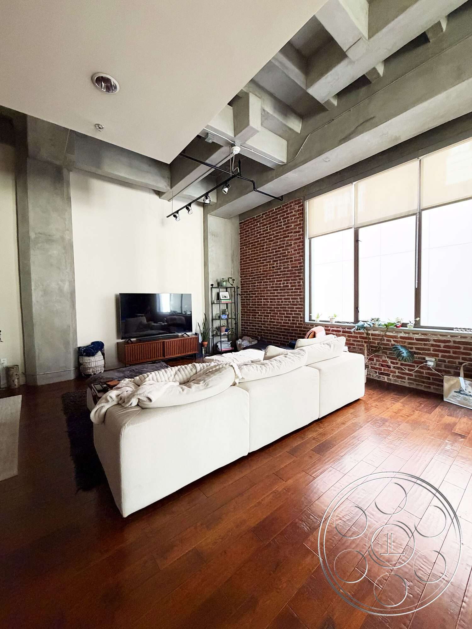 Brockman 310 - large windows, concrete ceiling, hardwood living room floors, recessed lighting fixtures, exposed brick accent wall, modern television stand, contemporary rug, minimalist sofa