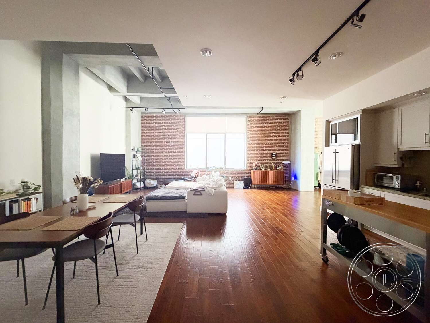 Brockman 310 - hardwood flooring, textured wall finish, modern dining table, contemporary living space, open floor plan interior, exposed brick accent wall, track lighting fixtures, industrial style architecture, steel chair legs, white kitchen cabinetry, concrete column, large factory-style windows