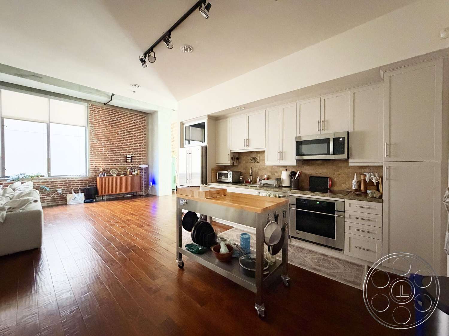 Brockman 310 - open concept living space, stainless steel kitchen appliances, hardwood living room floors, marble kitchen backsplash, exposed brick accent wall, track lighting fixtures, white shaker kitchen cabinets, wood countertop island