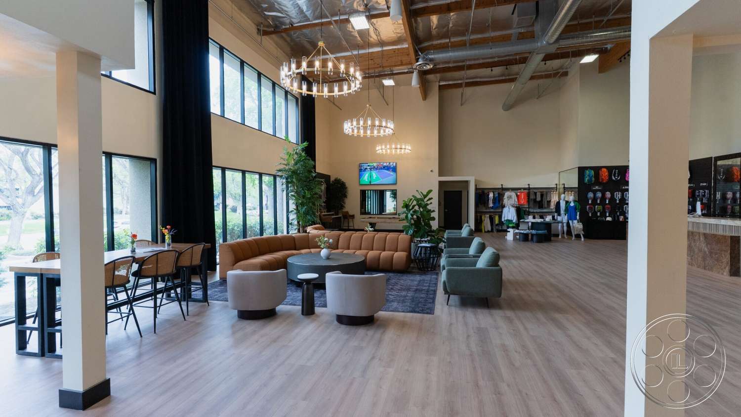 Gym 38 - neutral color palette, hardwood flooring, open concept layout, exposed wood beams, large floor-to-ceiling windows, cozy lounge area, modern sectional sofa, contemporary accent chairs, circular chandelier lighting, stone reception counter, black display wall with apparel