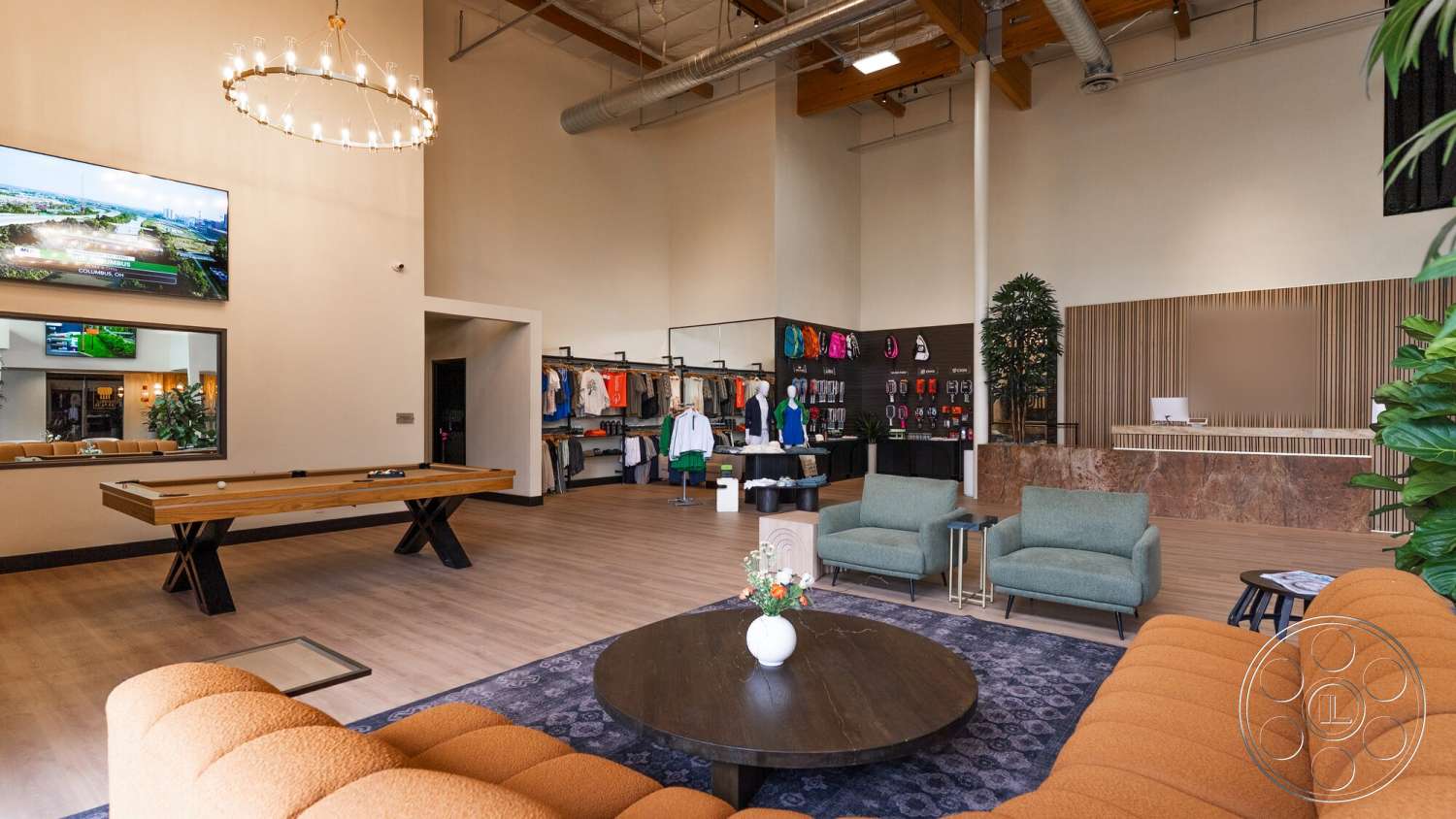 Gym 38 - open layout, textured wall panels, hanging plants, modern chandelier, pool table, orange fabric sofa, rectangular coffee table, brightly lit space, exposed wood ceiling beams, wall-mounted flat-screen TV, clothing display rack, polished wooden flooring, light green upholstered chairs, marble reception counter, decorative rug with circular pattern, community lounge area