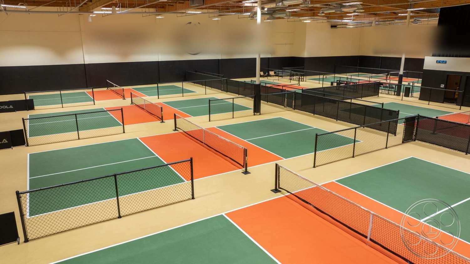 Gym 38 - high ceilings, wooden ceiling beams, interior sports facility, green and orange tennis courts, synthetic court flooring, black chain link fencing, colored court lines, multipurpose court layout, artificial turf sections