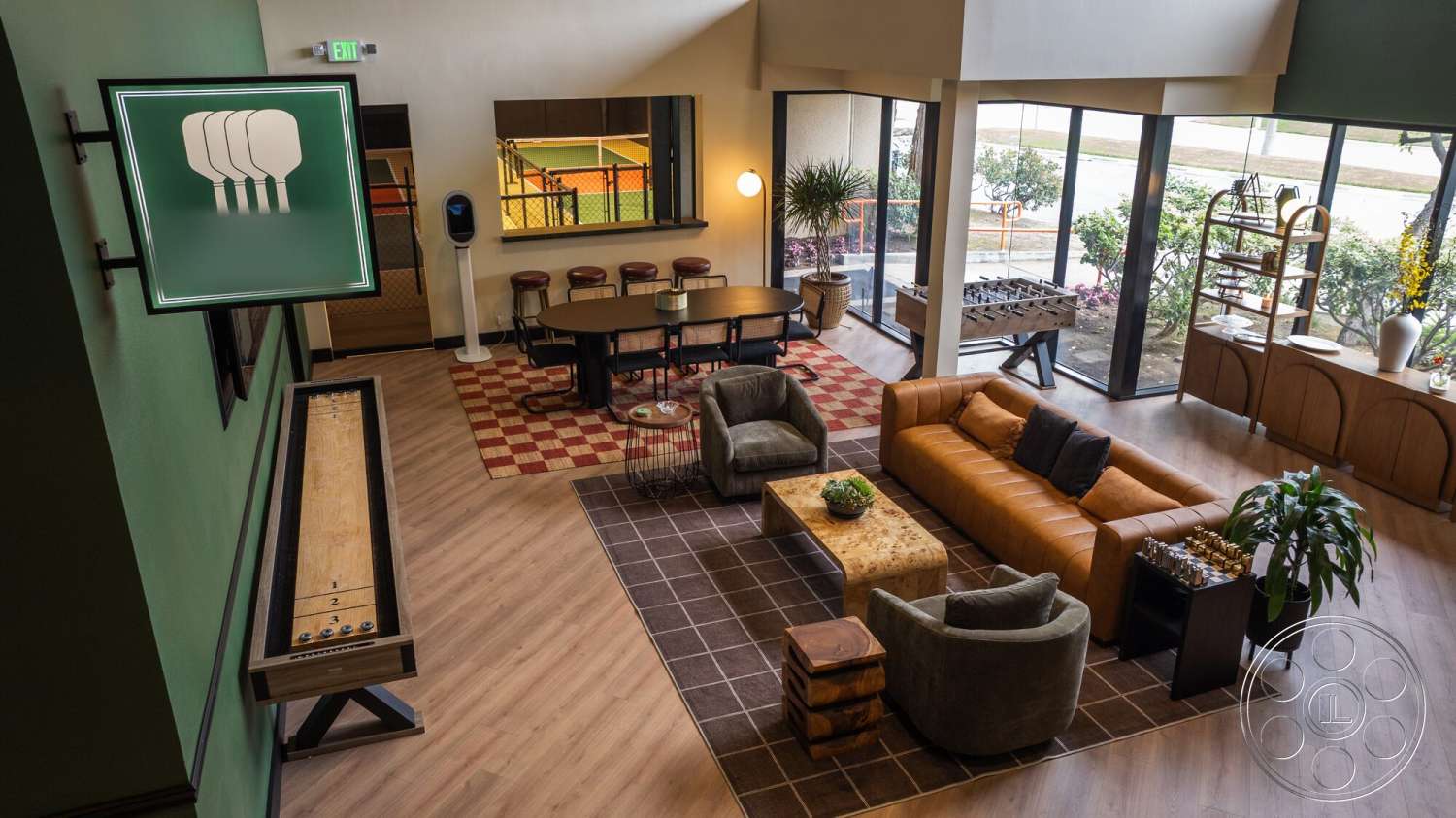 Gym 38 - open concept layout, plaid area rug, modern light fixture, rectangular coffee table, brown leather sofa, wood laminate flooring, green painted walls, glass sliding windows, grey upholstered armchairs, wooden game table, metal and wood shelving unit