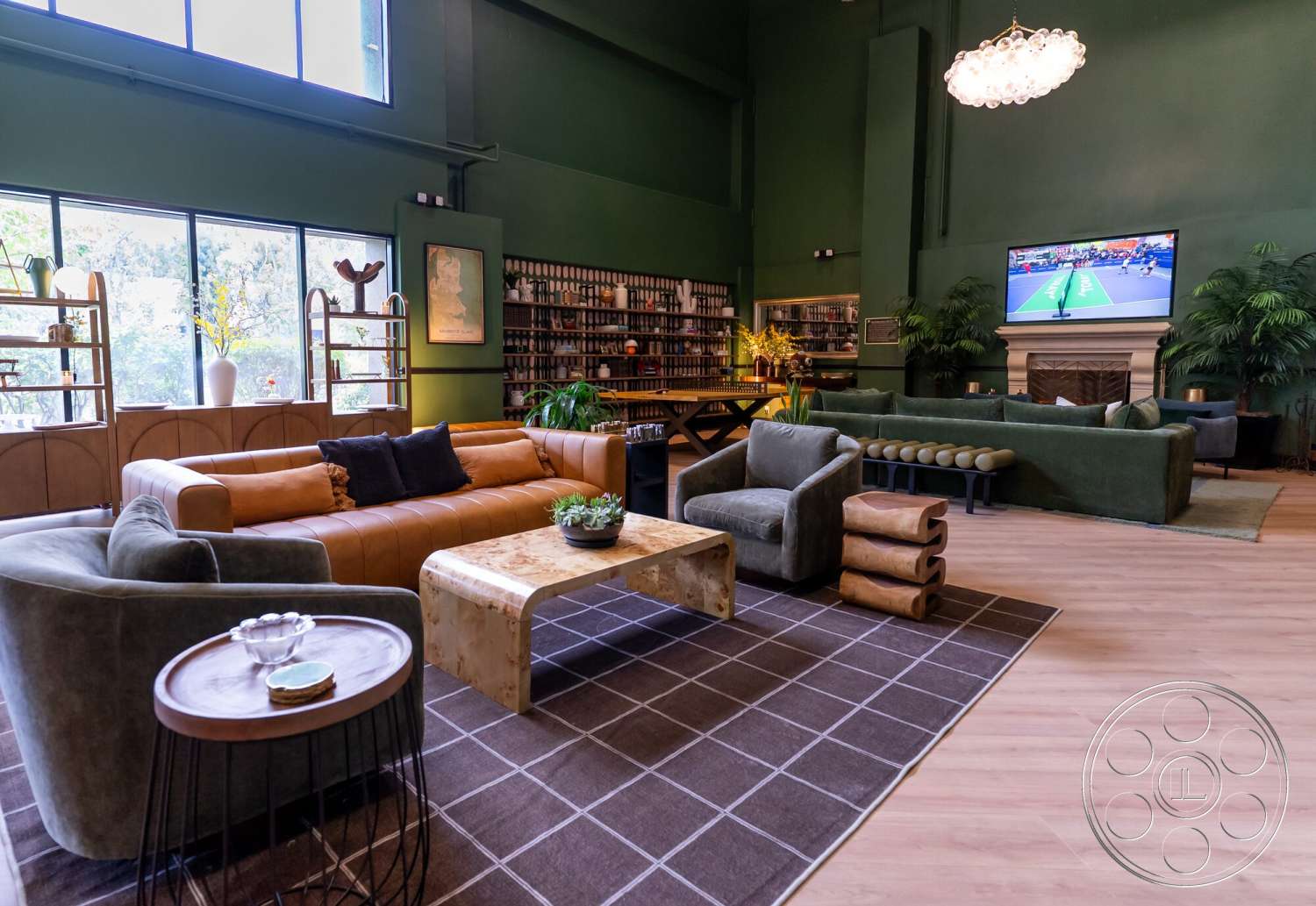 Gym 38 - hardwood flooring, open floor plan, floor-to-ceiling windows, light wood accents, geometric area rug, leather sofa, modern chandelier, lush indoor plants, stone fireplace surround, plush velvet armchairs, decorative shelving unit, green painted walls, reclaimed wood coffee table