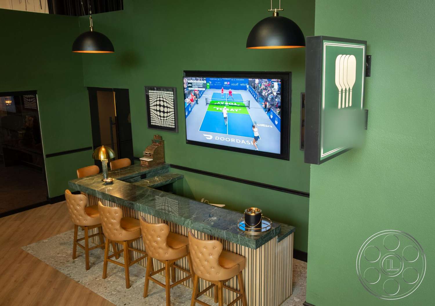 Gym 38 - hardwood flooring, open layout, textured wall treatment, flat-screen television, modern lounge area, metal pendant lighting, marble bar countertop, green painted walls, upholstered bar stools, black wall accents, built-in wall decor, striped bar base