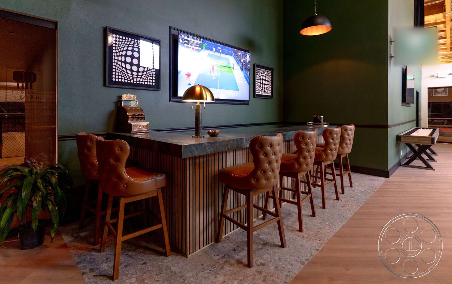 Gym 38 - wooden bar stools, decorative wall art, vinyl plank flooring, marble countertop bar, green painted accent walls, tan leather upholstery, wood paneling on bar front, light fixture with black metal shade, flat-screen TV on wall