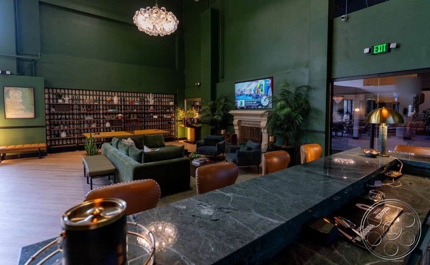 Gym 38 - contemporary style, casual seating area, hardwood floor, modern chandelier, large flat-screen TV, dark green walls, built-in shelving units, stone fireplace surround, potted indoor plants, upholstered lounge chairs, marble bar countertop, cozy lounge atmosphere, leather club chairs, light sconces