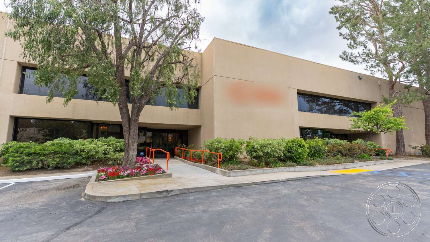 Gym 38 - exterior, modern architecture, large glass windows, mature trees, concrete walkway, asphalt parking lot, landscaped garden area, stucco building facade, decorative shrubbery, ornamental flower beds, orange railings